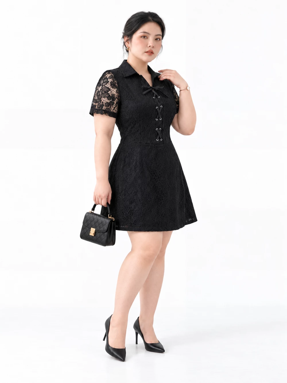 Angled model view of the black V-DA248 lace dress, hem above the knees, with black bag and shoes