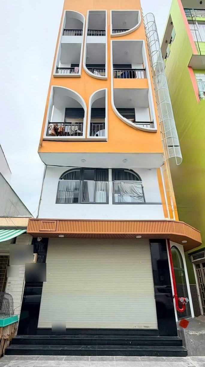 Mặt tiền tòa nhà sơn cam nhiều tầng, ban công bo cong, tầng trệt cửa cuốn