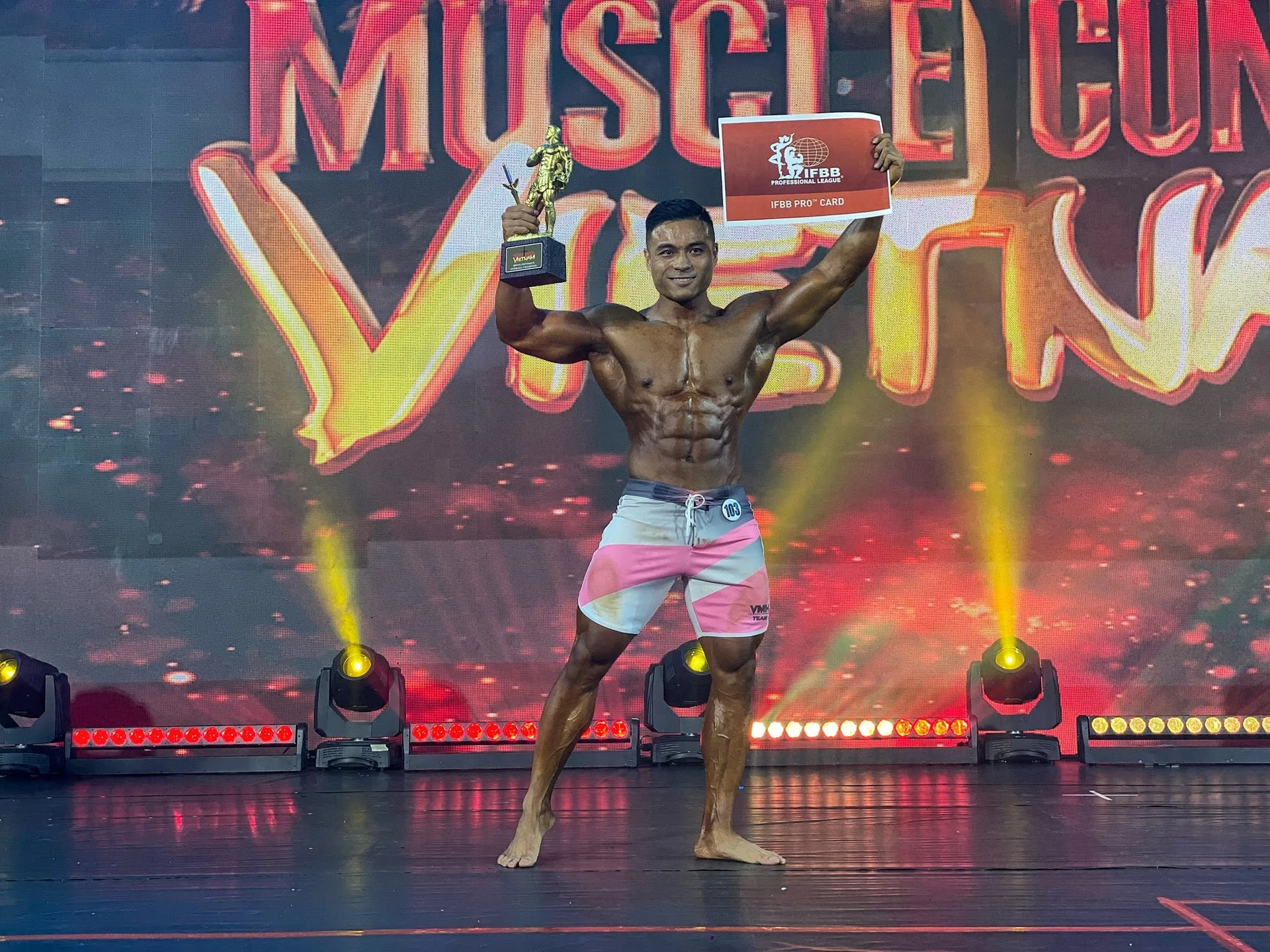 Vũ Minh Hiếu nâng cúp và bảng IFBB Pro Card, số báo danh 103